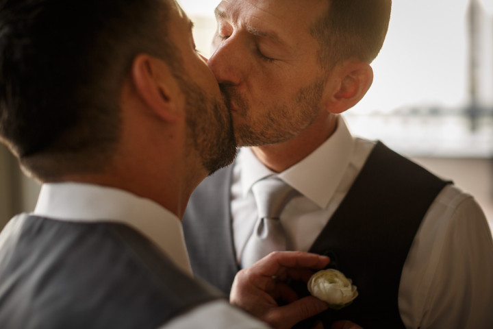 grooms kiss while getting dressed by Chicago gay wedding photojournalist