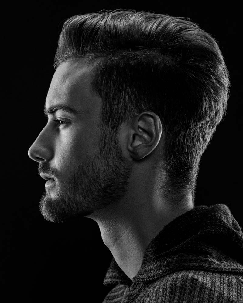 male model side profile with edge lighting on black backdrop shot in black and white