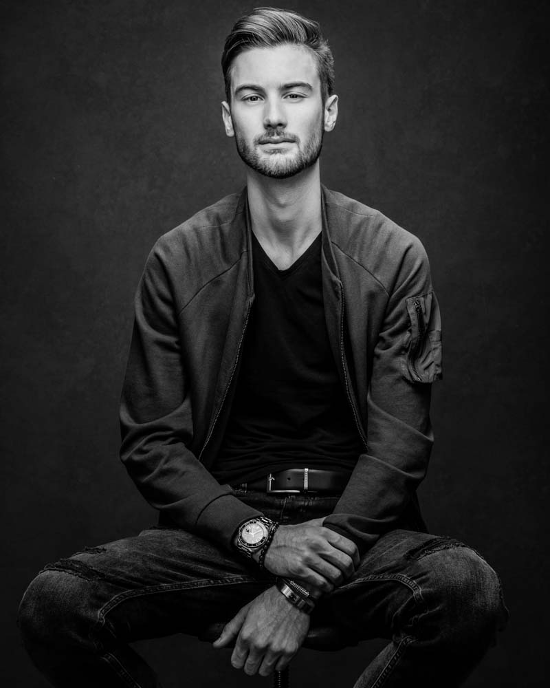 male model wearing jacket sitting on stool in black and white
