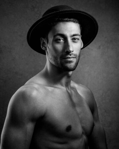 black and white headshot of shirtless male model wearing a hat the photo has beautiful side lighting and edge light