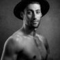 black and white headshot of shirtless male model wearing a hat the photo has beautiful side lighting and edge light