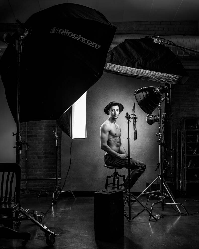 black and white headshot of shirtless male model wearing a hat the photo has beautiful side lighting and edge light behind the scenes 