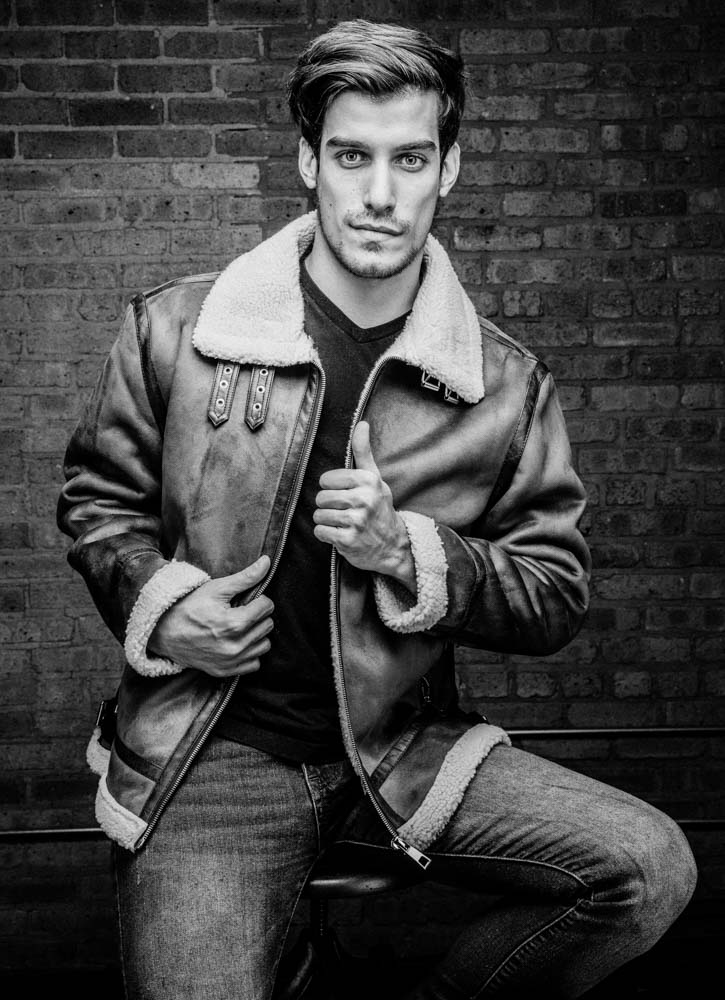 Male model in a leather jacket with a brick wall background in black and white