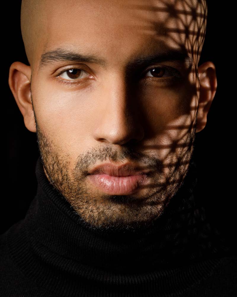a up close headshot of a male model with shadows on the side of his face casted by light shining through grid