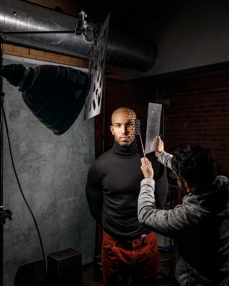 a up close headshot of a male model with shadows on the side of his face casted by light shining through grid behind the scenes