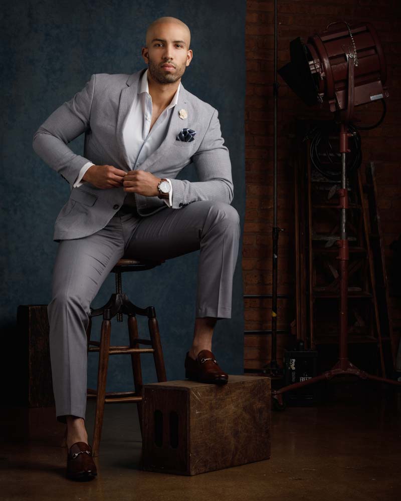 male model posed in a grey suit wearing watch next to movie props
