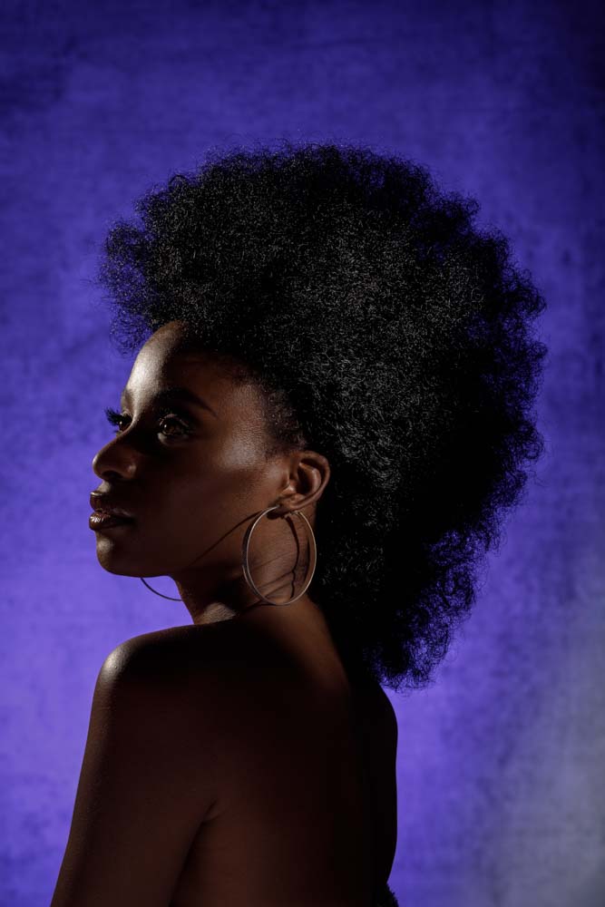 female model in front of a purple background illuminated by edge lighting that creates a beautiful gradient on her skin