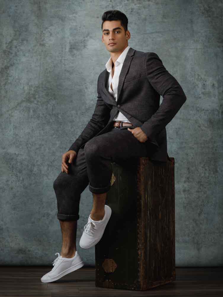 Akshay poses in a full-body shot against a light blue-gray textured canvas, illustrating how background choice can elevate the visual appeal and depth of professional headshots.