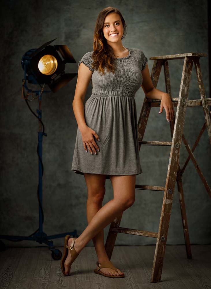 Taylor leaning on a wooden ladder with vintage props and soft lighting