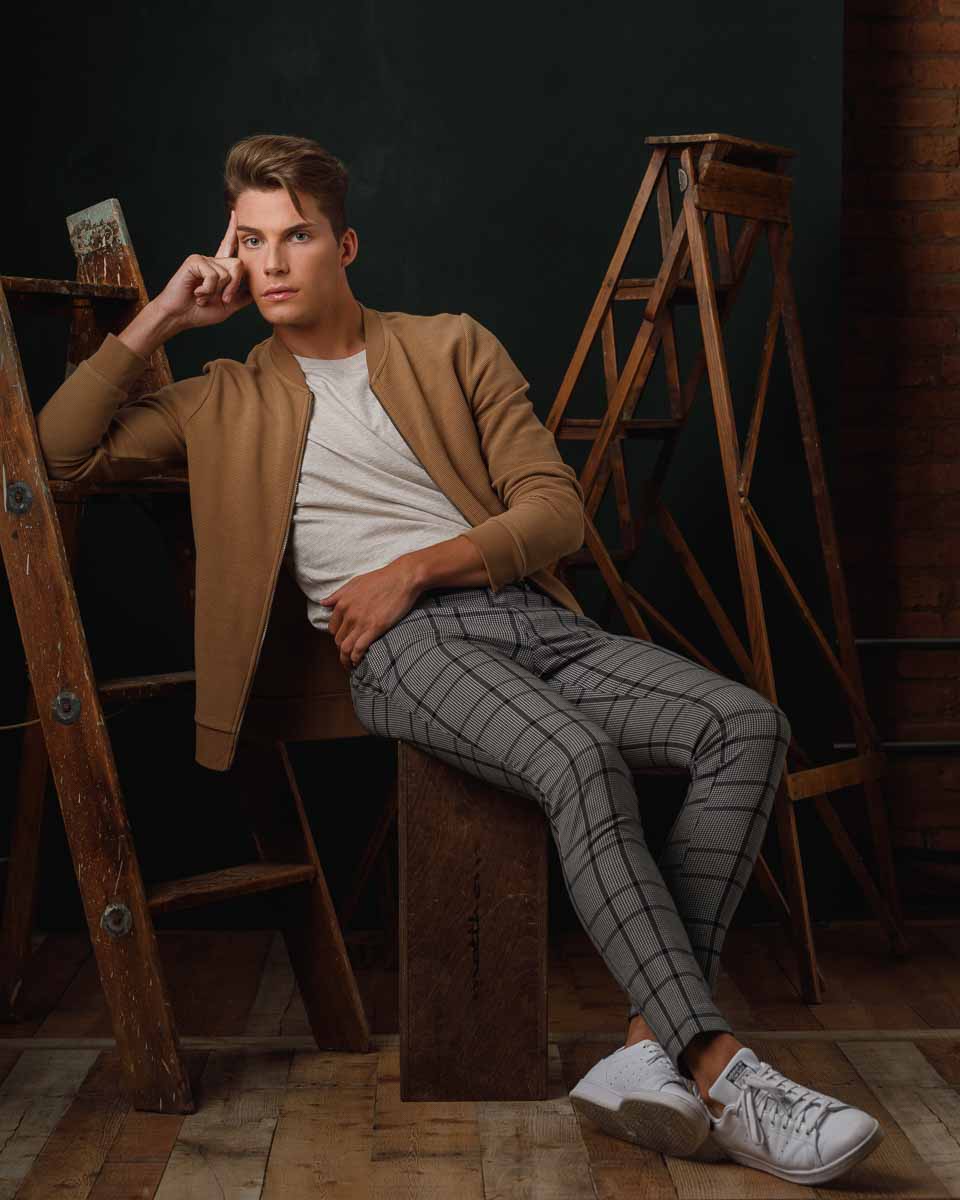 Full body portrait of Christian sitting on an apple box wearing white tennis shoes, plaid pants, and a white shirt