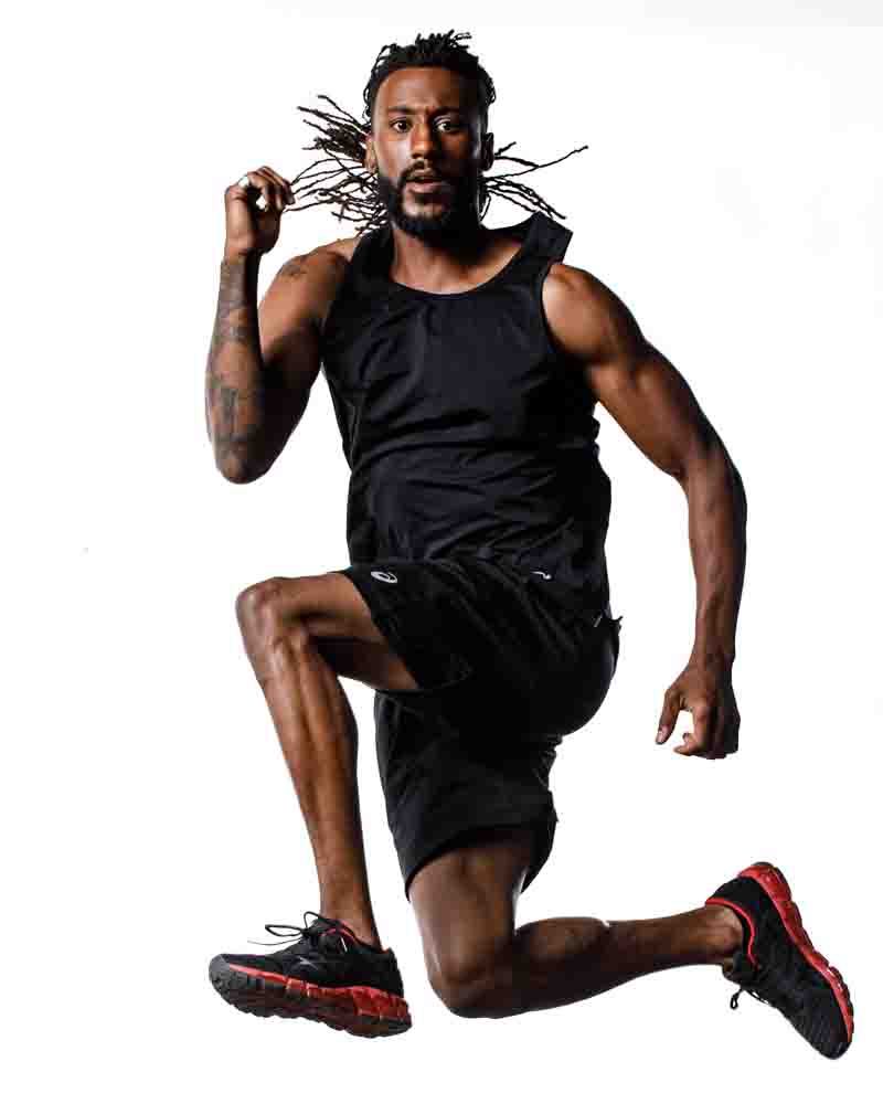 Chicago portrait photographer captures Matthew in action, jumping through the air in a fitness pose, wearing a black tank top, shorts, and black and red gym shoes, demonstrating athleticism and energy.