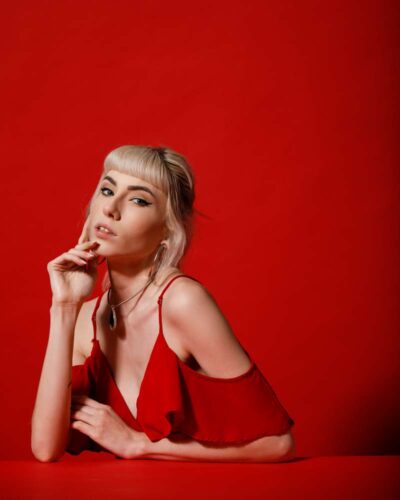 A freelance model photographer in Chicago captures Gabriella in a dramatic red dress leaning on a red table in front of a red background