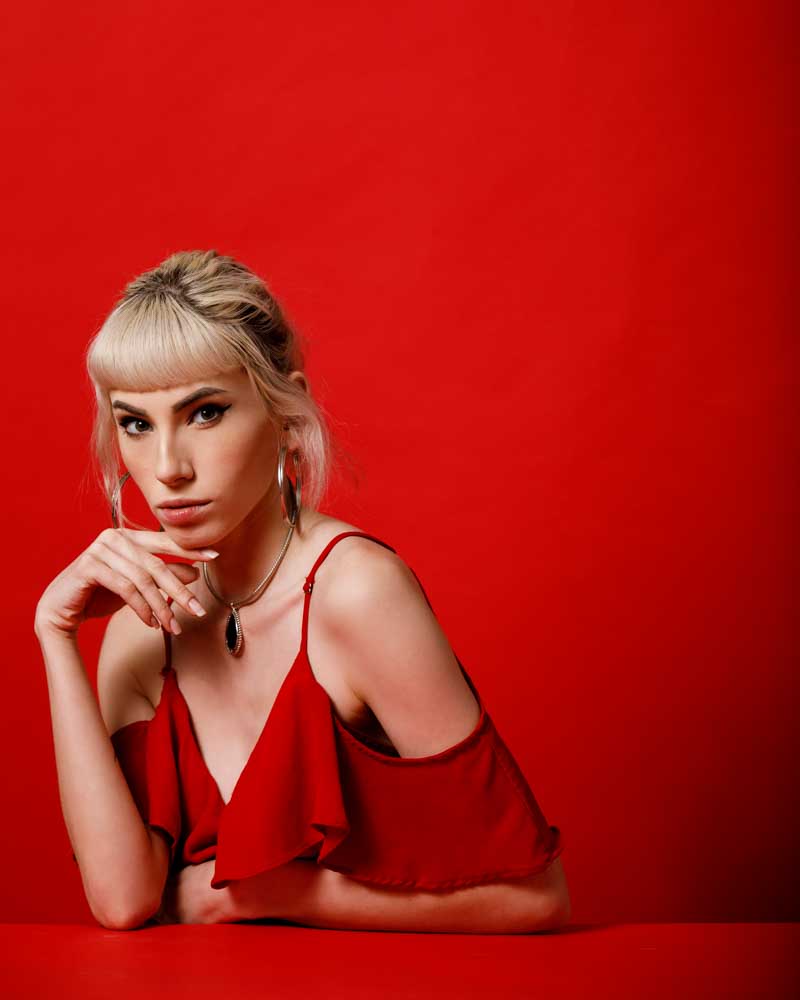Gabriella in a red dress in a dramatic pose against a red background
