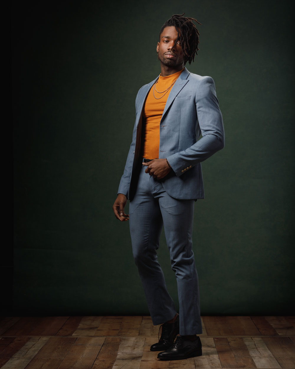 Prince in a blue suit and orange shirt in front of a green backdrop, exemplifying high-fashion model portfolio photography in Chicago by John Gress.