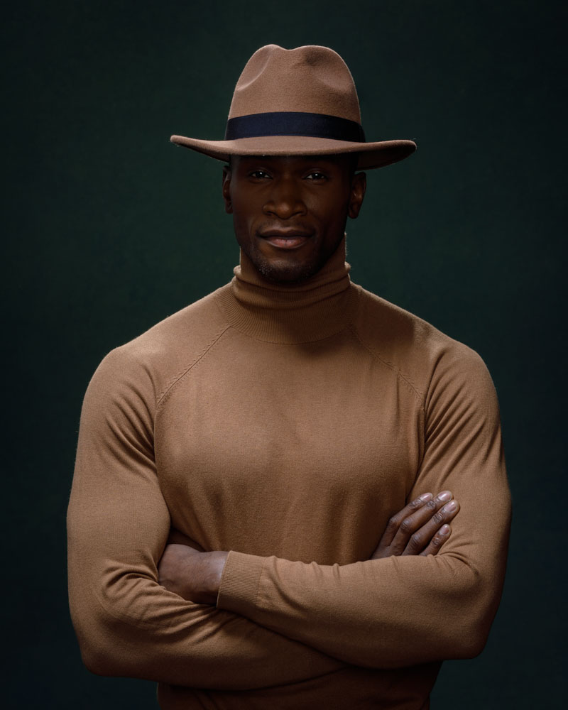 Artistic portrait of Chaun in a brown turtleneck and hat under dramatic lighting, capturing the essence of his modeling prowess in Chicago.