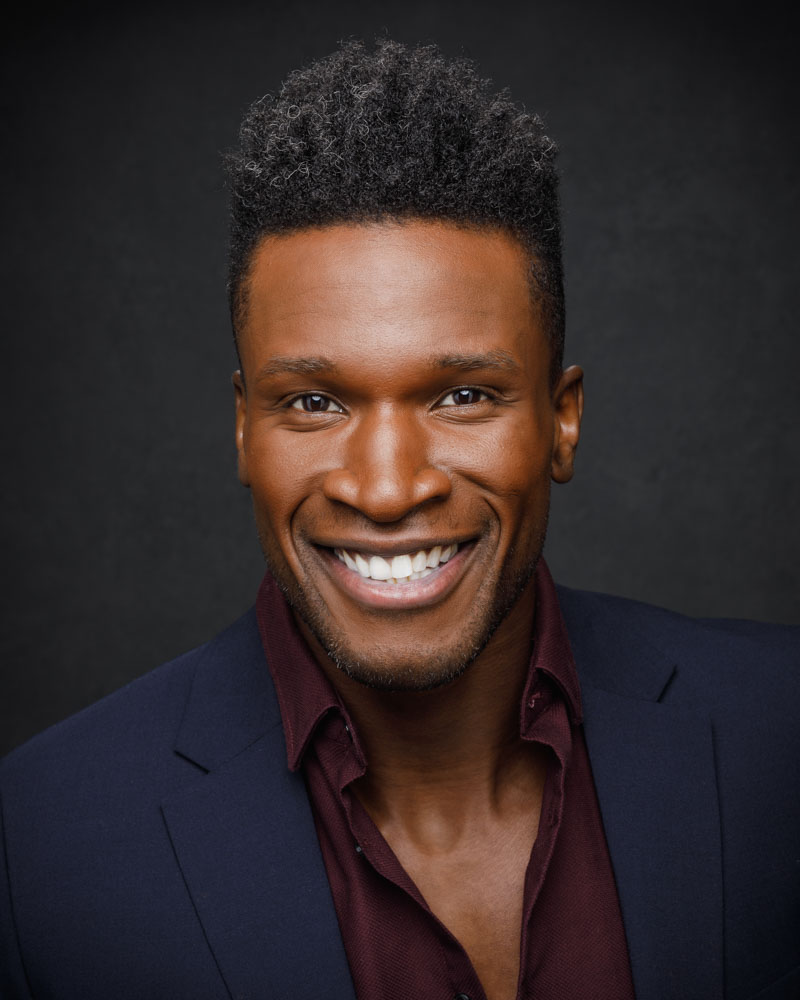 Chaun in a blue suit with a maroon shirt, smiling in front of a gray canvas backdrop captured during his modeling portfolio service in Chicago