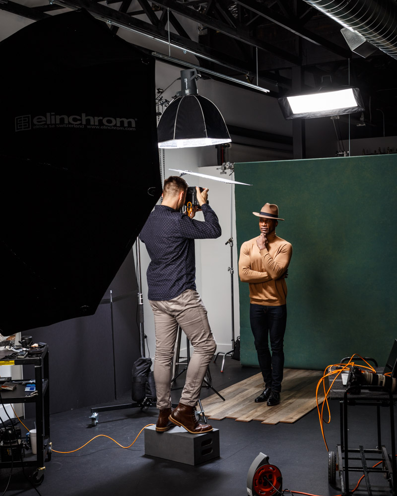 Behind the scenes image of John Gress capturing a headshot of Chaun in a brown turtleneck sweater and matching hat with the light coming from above and a shadow on his face during his modeling portfolio service in Chicago