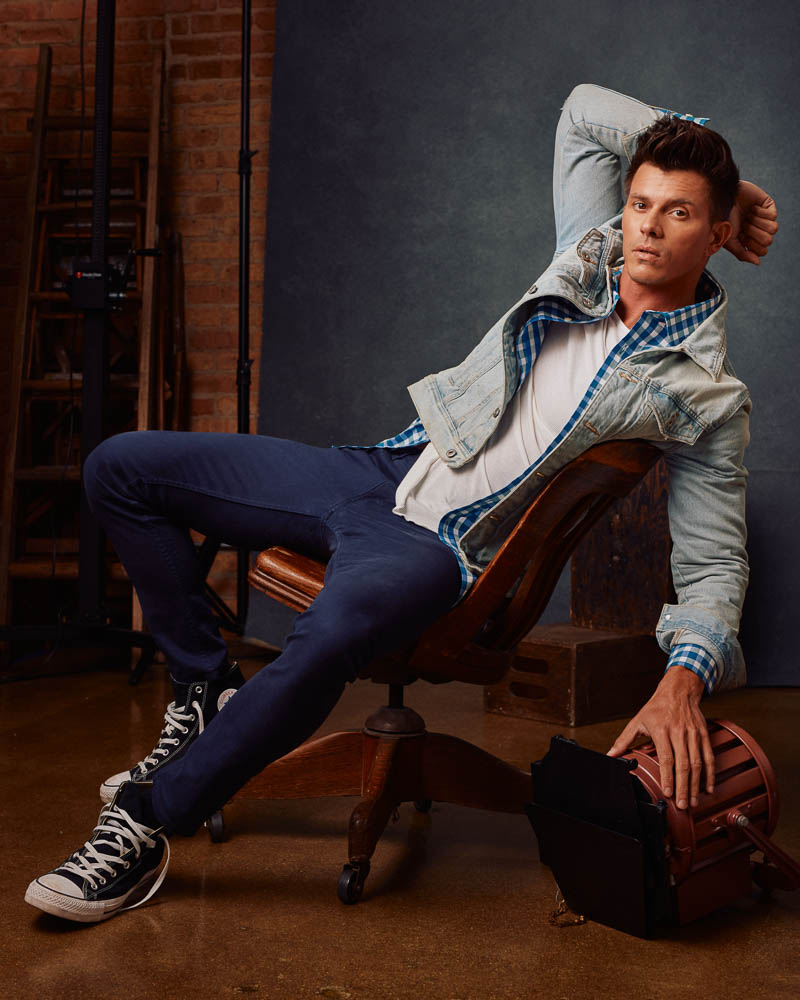 Kenny, leaning back in a wooden chair, showcases his casual style in this relaxed yet professional photoshoot by John Gress Photography in Chicago.