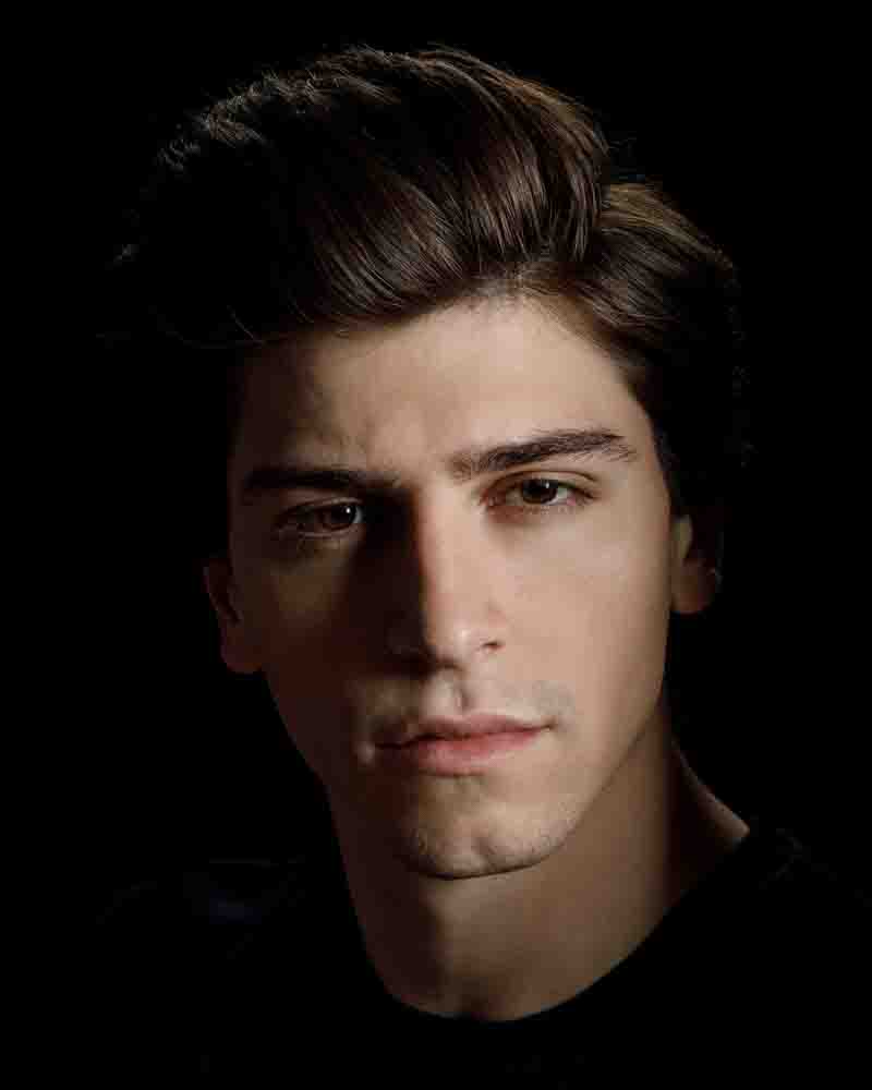 Dramatically lit headshot of Noah with a pure black background, emphasizing his features for theatrical roles.