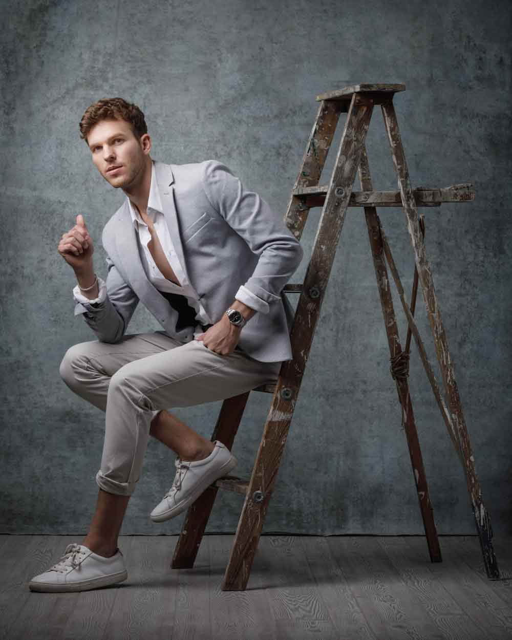 Connor seated on an antique wooden ladder in a gray suit
