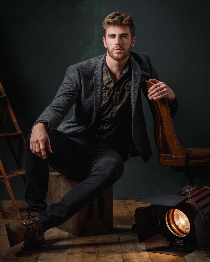 Jay in a full body portrait wearing brown boots and a tweed suit jacket, portraying a sophisticated yet approachable style.