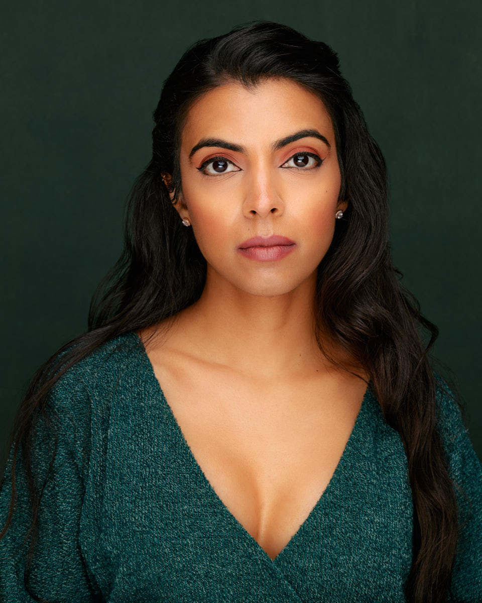Sana’s headshot captures her with a neutral expression, looking straight into the camera. She is wearing a teal top, and the dark green background enhances the contrast.