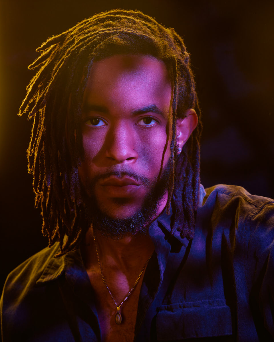 Jalen's portrait slightly farther away, shows him in the same dramatic lighting with pink and yellow hues, wearing a dark shirt and a pendant necklace.