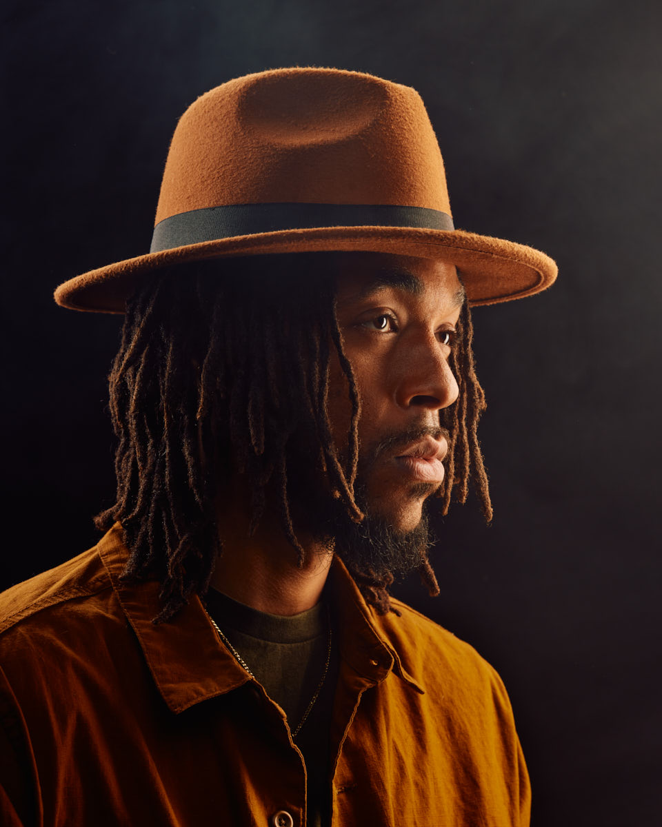 Jalen in a Chicago model photo studio, looking to the side, wearing a brown hat and a brown shirt, with soft, warm lighting enhancing the mood.
