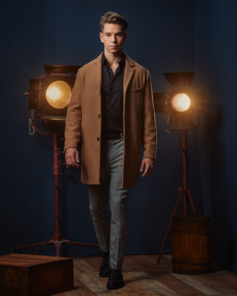 Erik standing confidently in a tan overcoat, demonstrating the versatility and professionalism of his portfolio