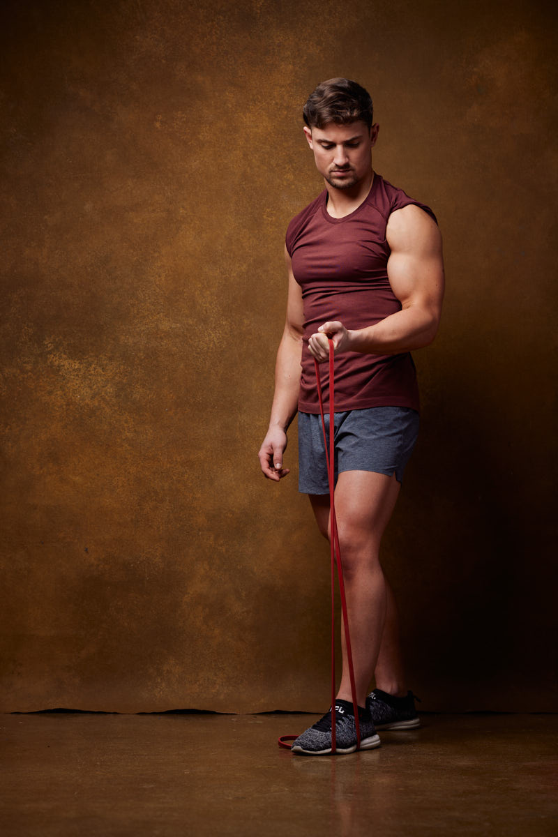 Fitness model Tom posing in a powerful stance, showcasing his toned physique and determination. The plain background emphasizes his muscular form and the intensity of his expression.