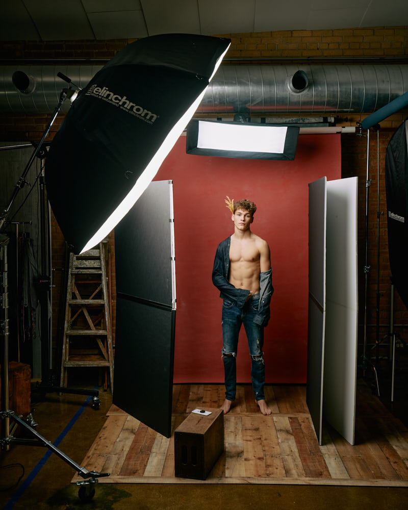 Evan behind the scenes on set, wearing a jean shirt and holding wheat