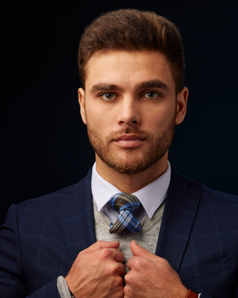 This is a headshot of Constantine in a blue suit, jacket and tie, looking at the camera