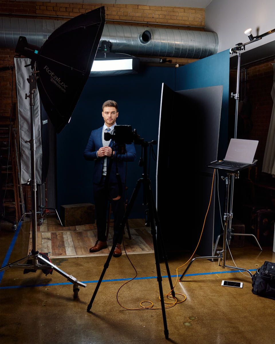 this is a behind the scenes photo of the following: This is a headshot of Constantine in a blue suit, jacket and tie, looking at the camera