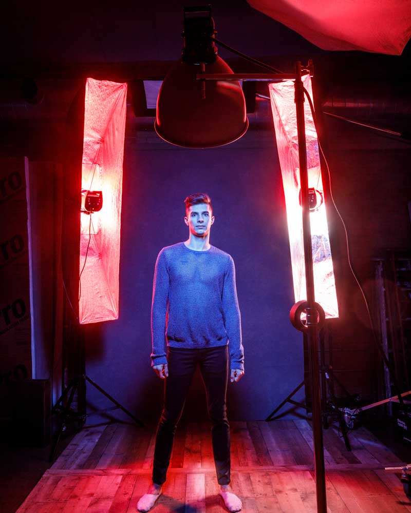 Michael is standing in the studio with an intense red and blue lighting setup. The behind-the-scenes shot shows the lighting equipment and the studio environment.