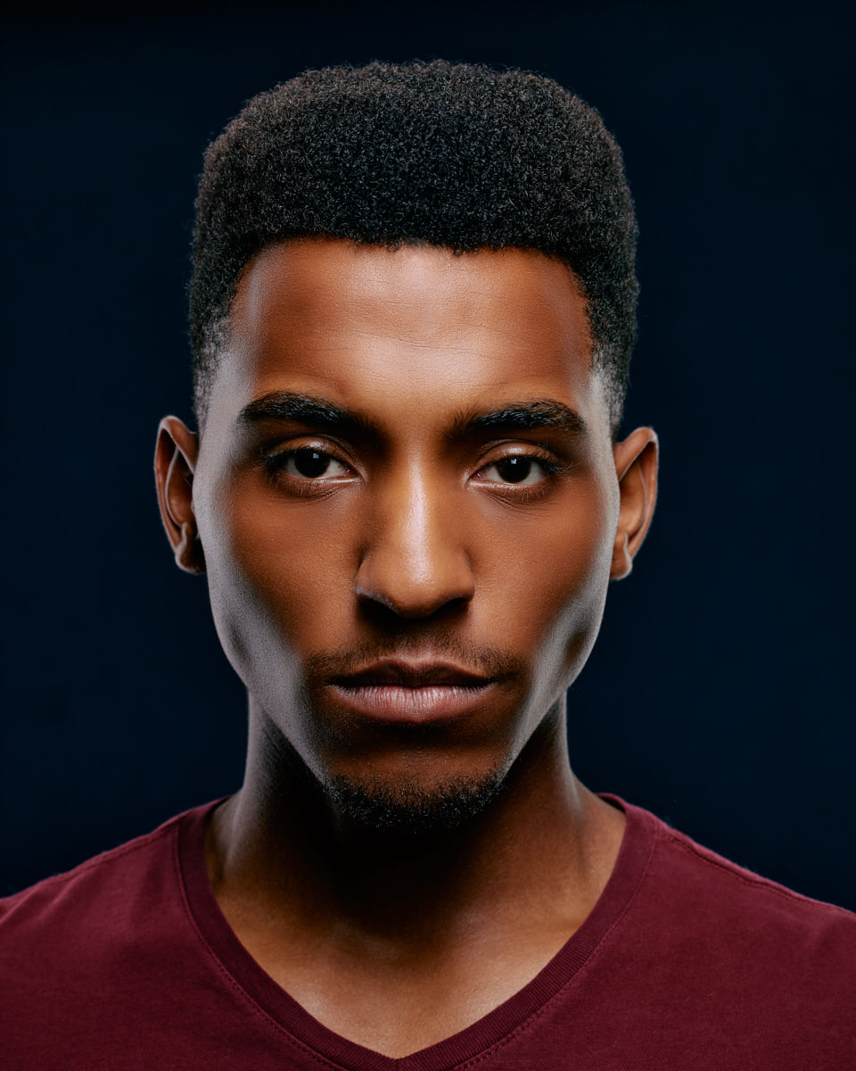 Justin's serious and confident look, highlighted by his short afro hairstyle and maroon V-neck shirt, makes this headshot ideal for dramatic roles.