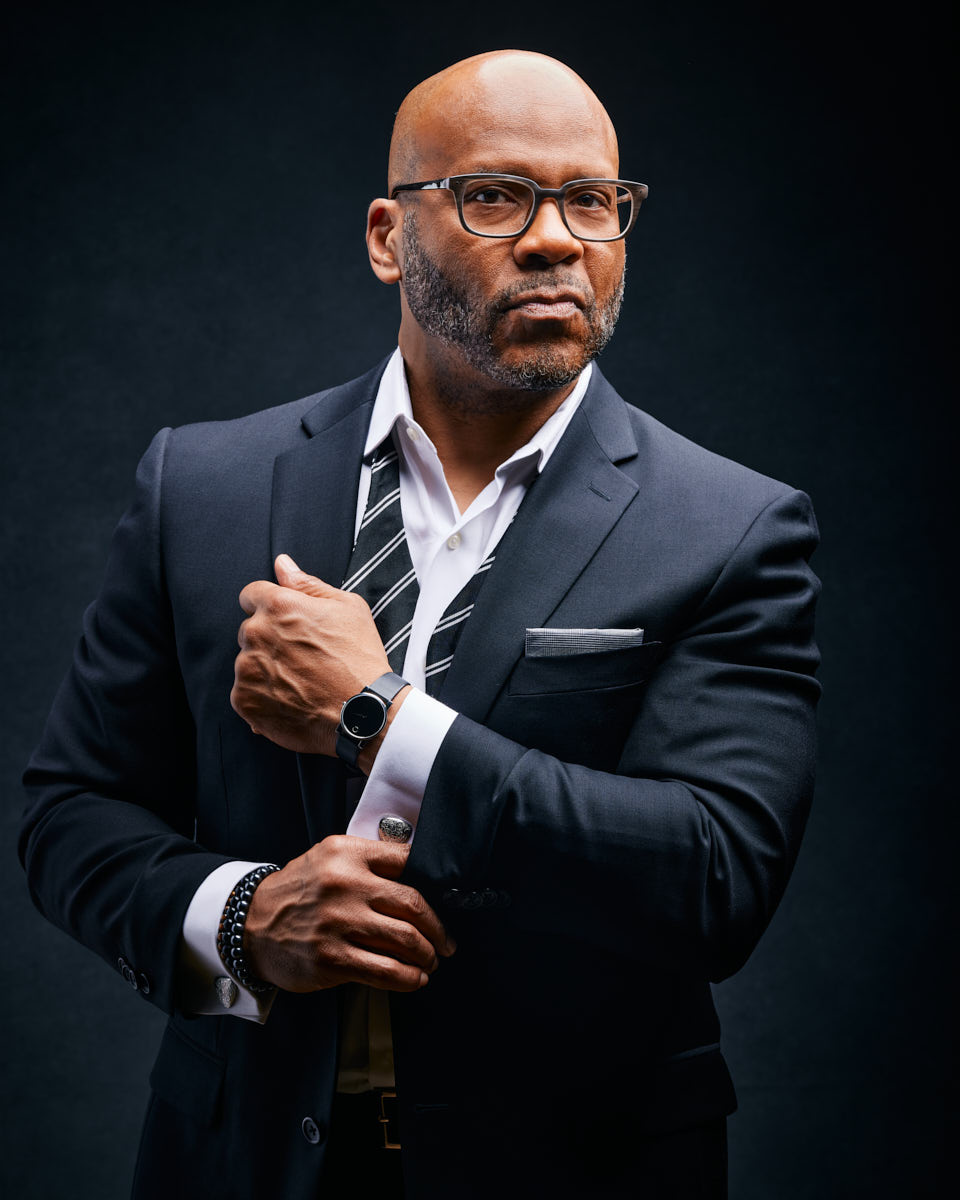 Michael exudes sophistication in a black suit with a striped tie. His pose is confident and polished, perfect for corporate branding. The dark background adds to the image's elegance and professional tone.