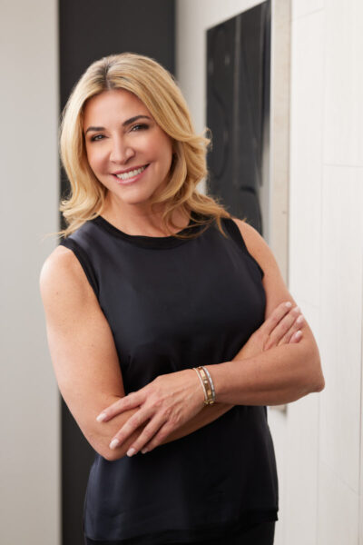When researching corporate portrait pricing in Chicago look for images like this one. Kate's portrait shows her in a sleeveless black top, with her blonde hair styled in loose waves. She is standing with her arms crossed, smiling confidently in what appears to be an office setting, adding a touch of approachability and professionalism to her image.