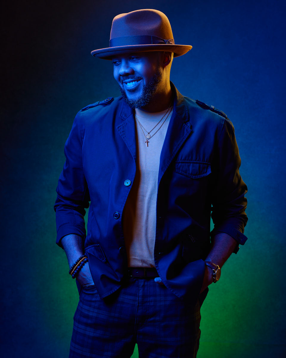 Under dramatic blue and green lighting, David smiles while posing with his hands in his pockets. The unique lighting and his casual attire make this a standout image in male model lookbook photography.