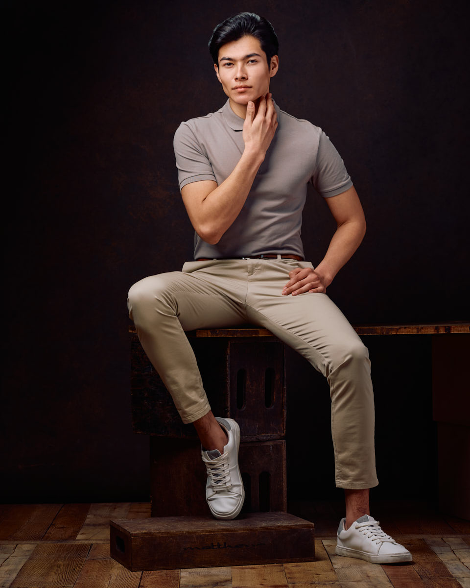 male model portfolio ideas in Chicago include this Full-body shot of Santiago sitting on a wooden box, wearing a grey polo shirt and beige pants with white sneakers. The warm, inviting background creates a rich atmosphere.