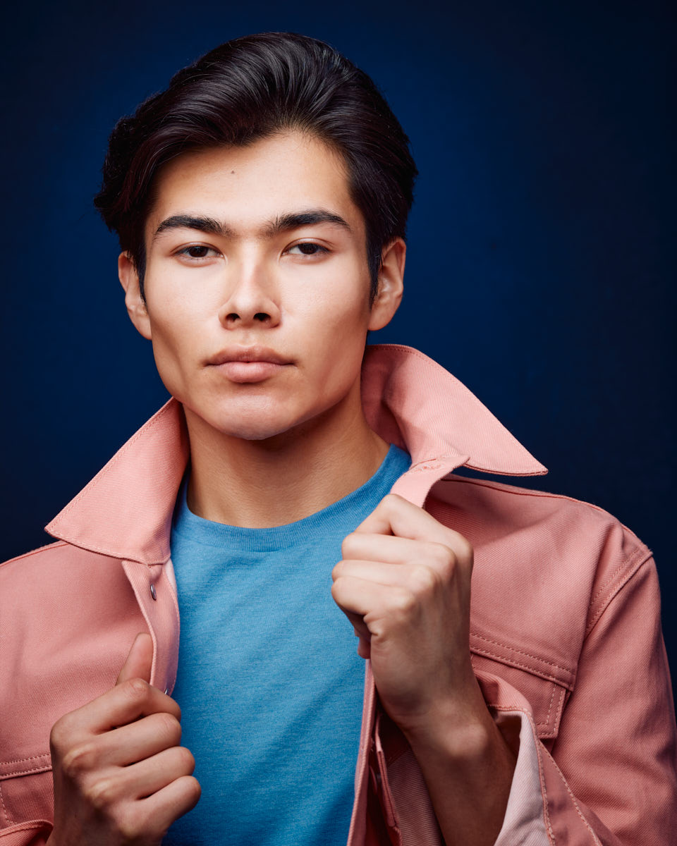 Another close-up of Santiago in the pink jacket and blue shirt, with a calm and composed facial expression. The blue background enhances the overall color palette of the image.