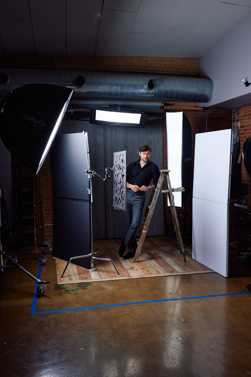 A wider shot of Stanislav in the studio setup. The environment showcases the professional lighting and backdrop used to create the sophisticated look. Stanislav is posing with the ladder, highlighting the behind-the-scenes aspect of the shoot