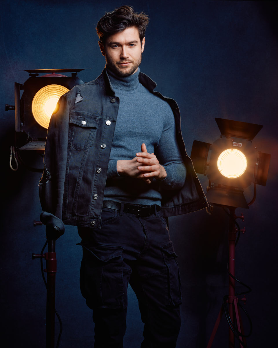 A closer shot of Stanislav in the same outfit, with a denim jacket draped over his shoulders. He is standing confidently in front of the studio lights, which provide a cinematic atmosphere. male model portfolio in Chicago