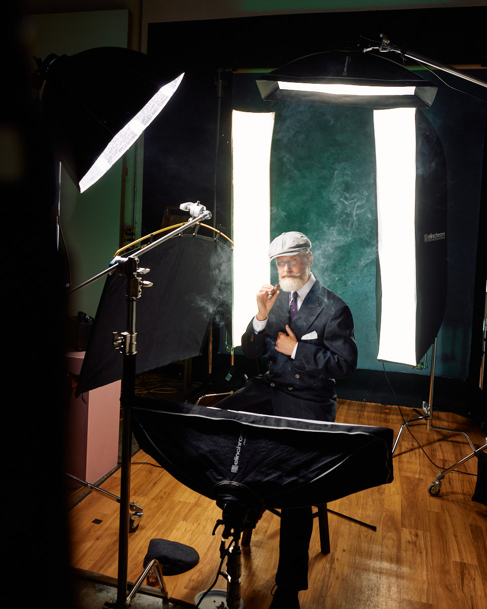 Behind-the-scenes image of Jeff in the studio, this time dressed in a suit and hat, holding a cigar, with a dramatic lighting setup and smoke effects, creating a classic and sophisticated atmosphere.