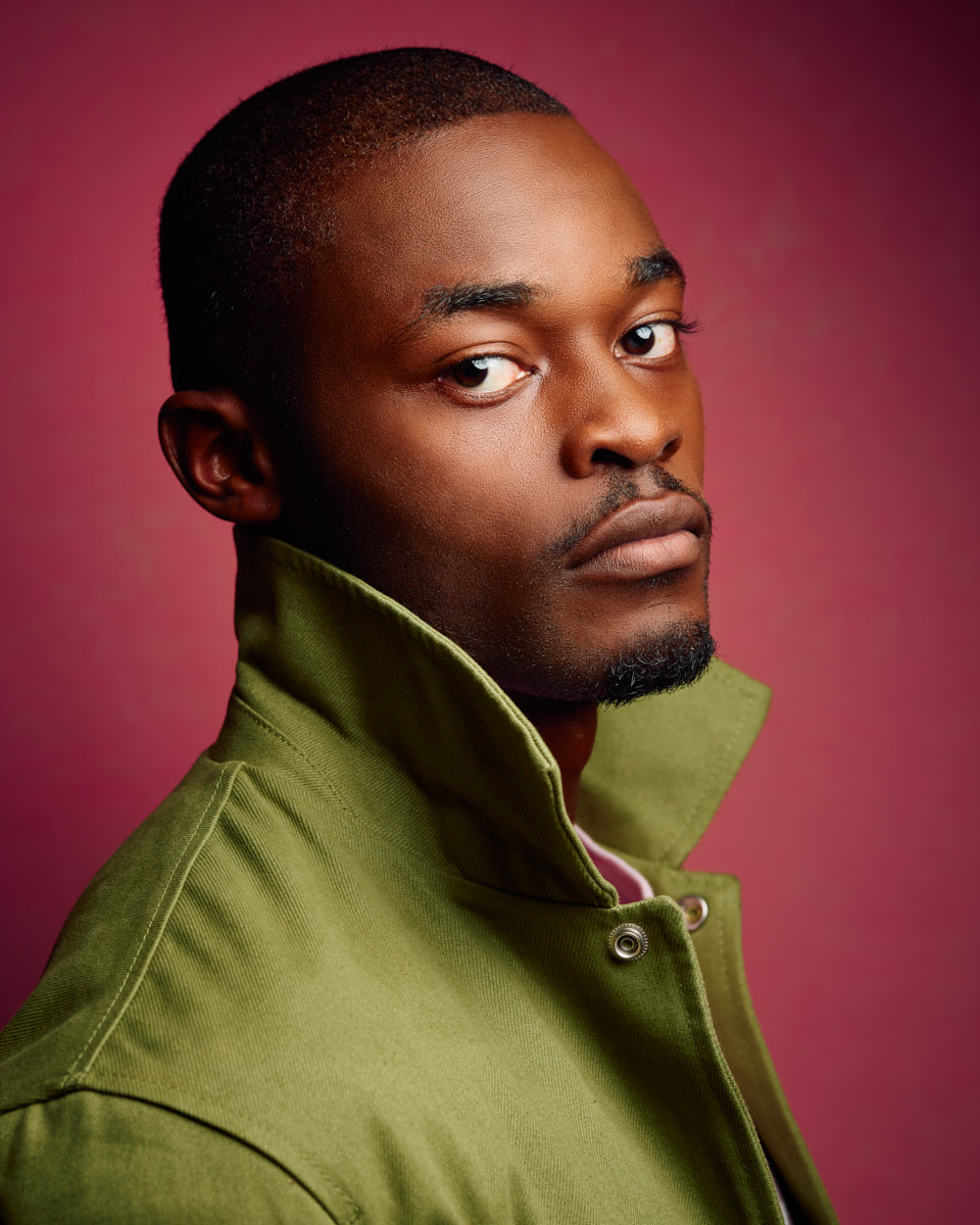 Chido poses against a pink background, wearing a green jacket with the collar turned up, giving a stylish and bold look.
