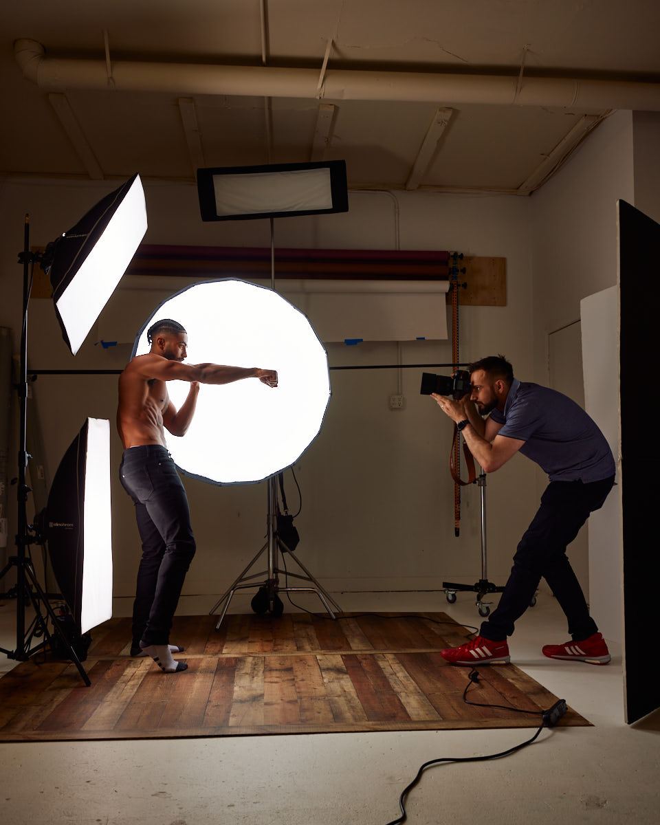 Shomari is posing in a professional photography studio. The setup includes several light sources: a large circular light behind Shomari, two softbox lights on either side, and a rectangular light overhead during Modeling Photoshoot in Chicago