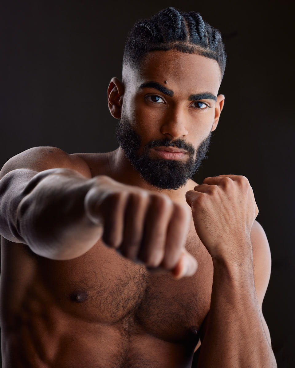 Shomari is captured in an intense and powerful pose during a Modeling Photoshoot in Chicago, throwing a punch directly towards the camera. His shirtless torso showcases his muscular build and defined abs