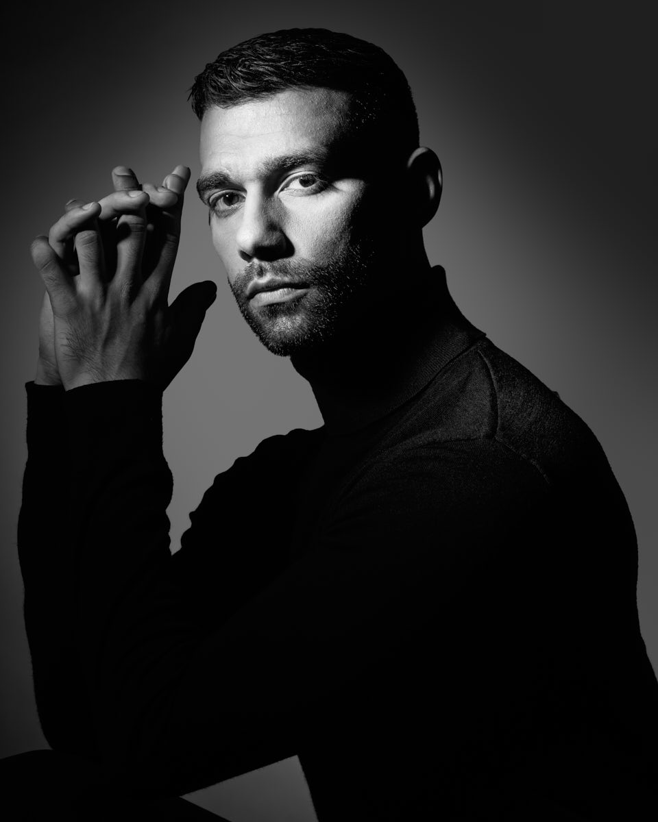Chicago Dance Photography-This black and white portrait captures Fernando in a more introspective pose. He has his hands clasped in front of his face, which is illuminated by a soft light, casting shadows that enhance his facial features.