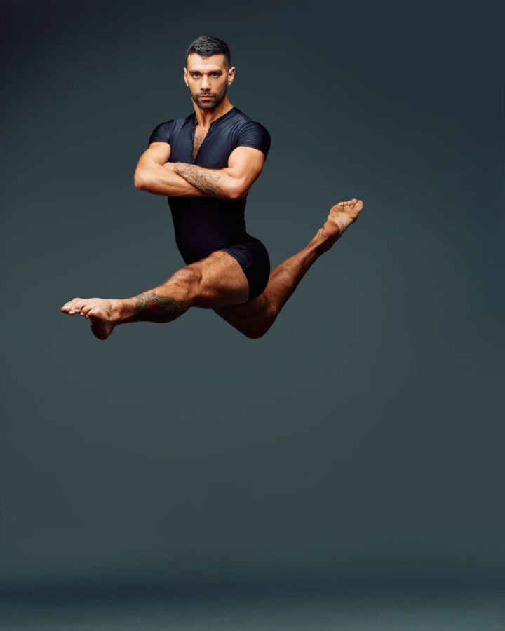 Another action shot of Fernando mid-air, this time with his arms crossed over his chest. His legs are in a split position, and he maintains a focused expression. His tattoo is visible on his leg, and the image captures the height and grace of his jump.