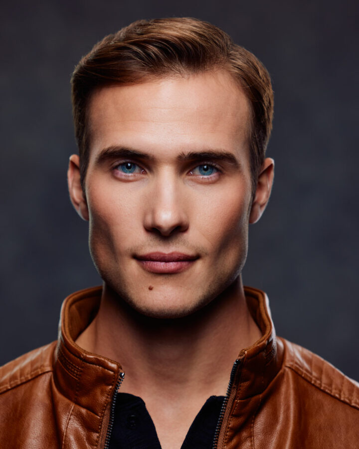 A model portfolio in Chicago close-up of David’s face in a leather jacket, showcasing his striking blue eyes and sharp features against a blurred background.