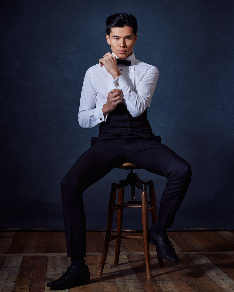 Become a Male Model in Chicago-Santiago sits on a stool, adjusting his bow tie with a composed and elegant demeanor, emphasizing his formal and sophisticated side.